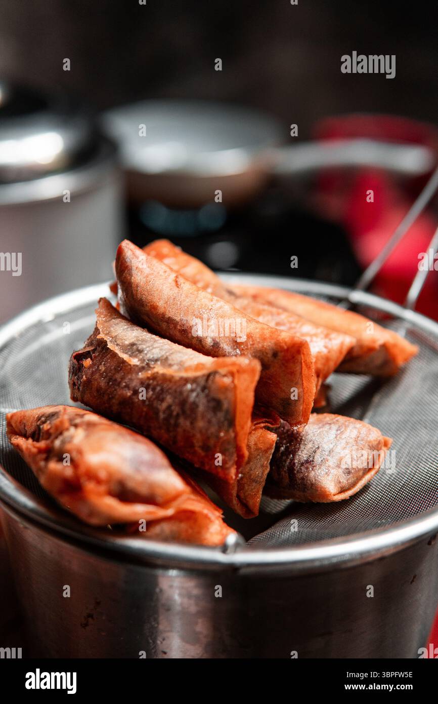 Rouleaux de printemps dorés croustillants égouttant l'huile sur une passoire en métal dans un cadre de cuisine maison. Parfait pour les thèmes culinaires, asiatiques ou culinaires. Banque D'Images