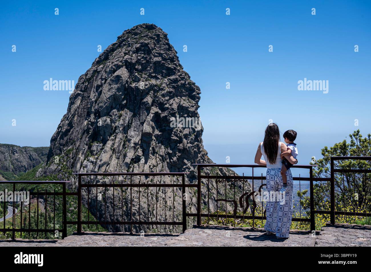 Une femme et un enfant sont debout sur un rebord, regardant au-dessus d'une grande montagne. La femme tient l'enfant, et ils semblent tous les deux profiter du Banque D'Images