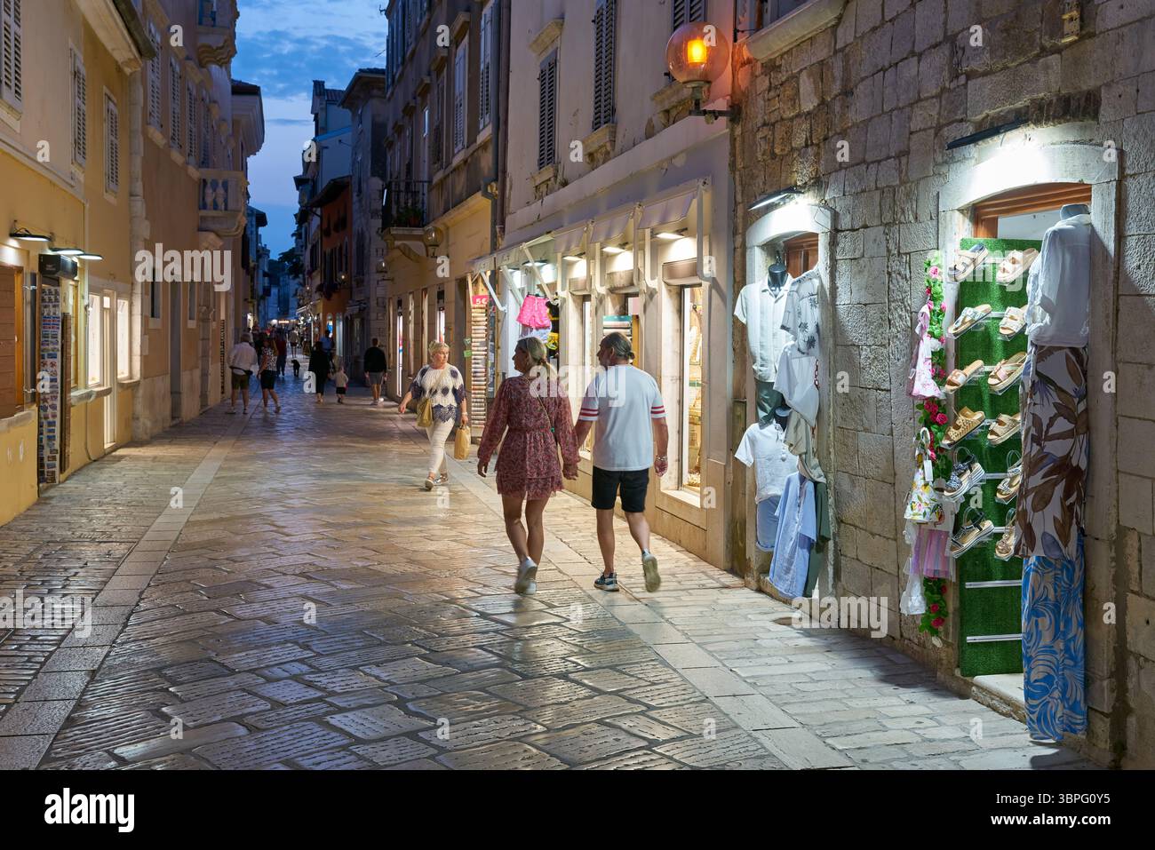 Ruelle avec des magasins et des touristes dans la vieille ville illuminée de Porec en Croatie dans la soirée Banque D'Images