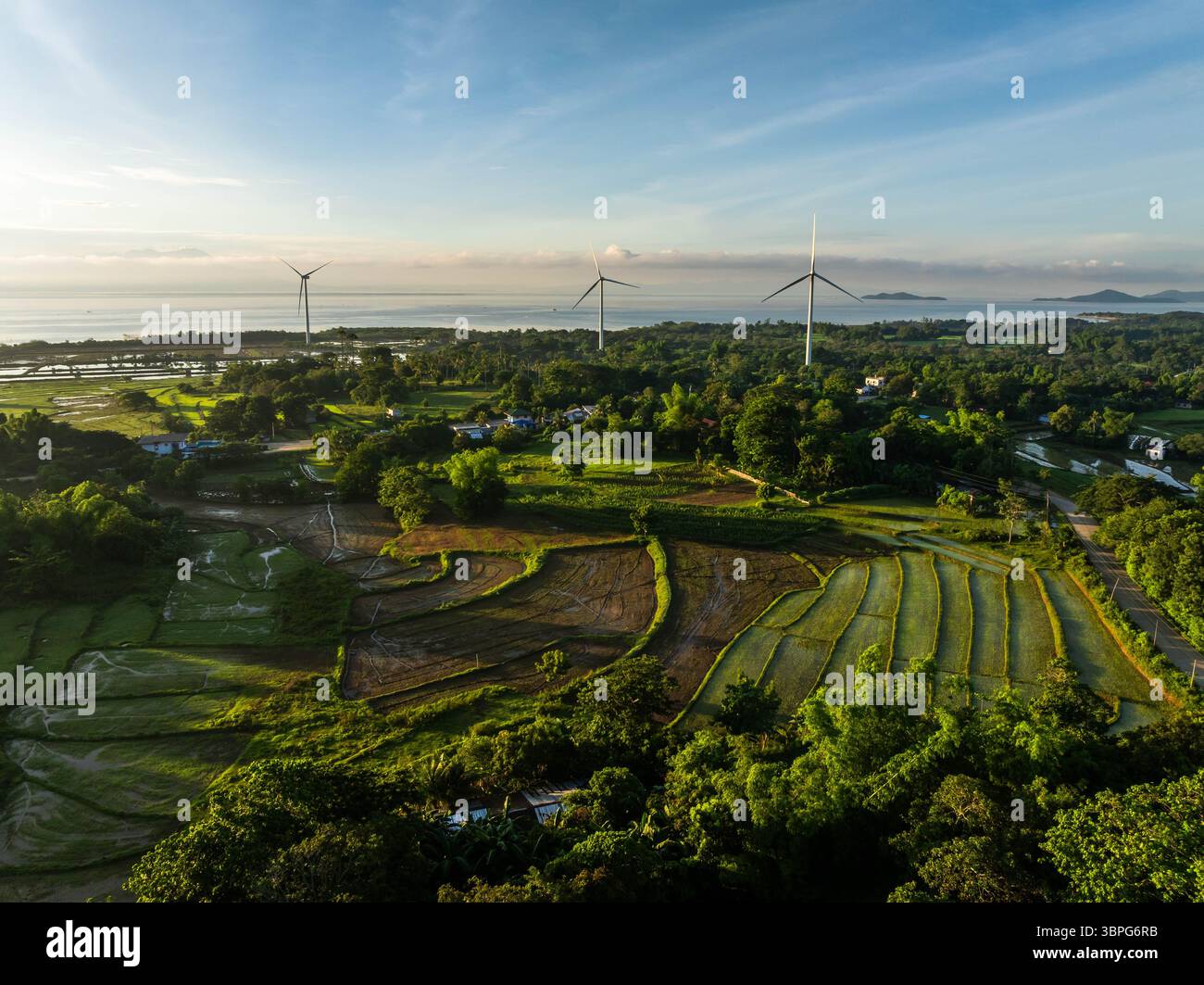Vue aérienne des éoliennes debout au milieu des champs verdoyants et des paysages côtiers, un contraste paisible de la technologie et de la nature, San Lorenzo, Guimaras, Philippines. Banque D'Images
