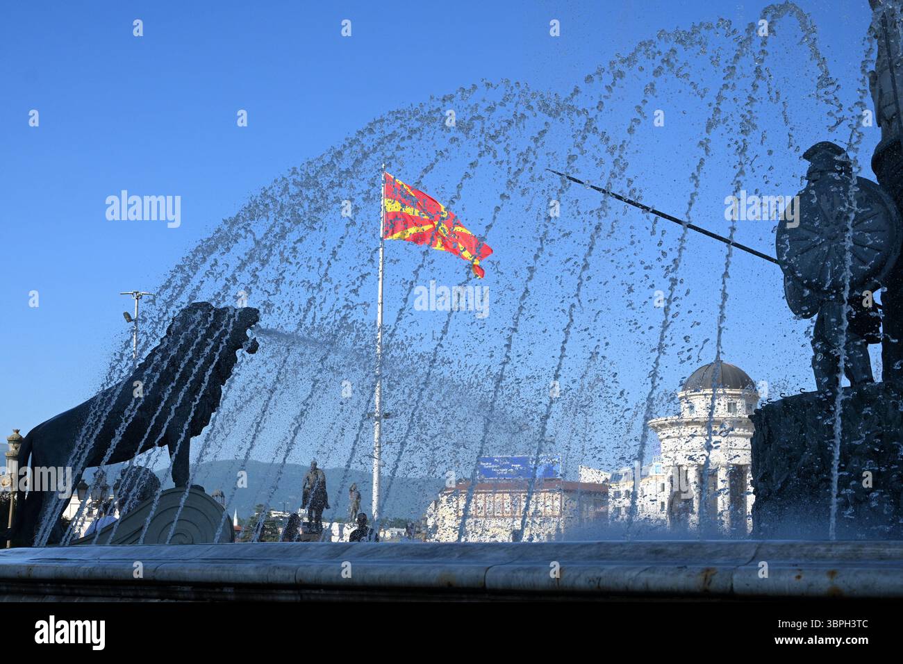 Skopje, Macédoine du Nord - 15 juin 2025 : drapeau de Macédoine du Nord et fontaine avec sculptures sur la place centrale de Skopje. Banque D'Images