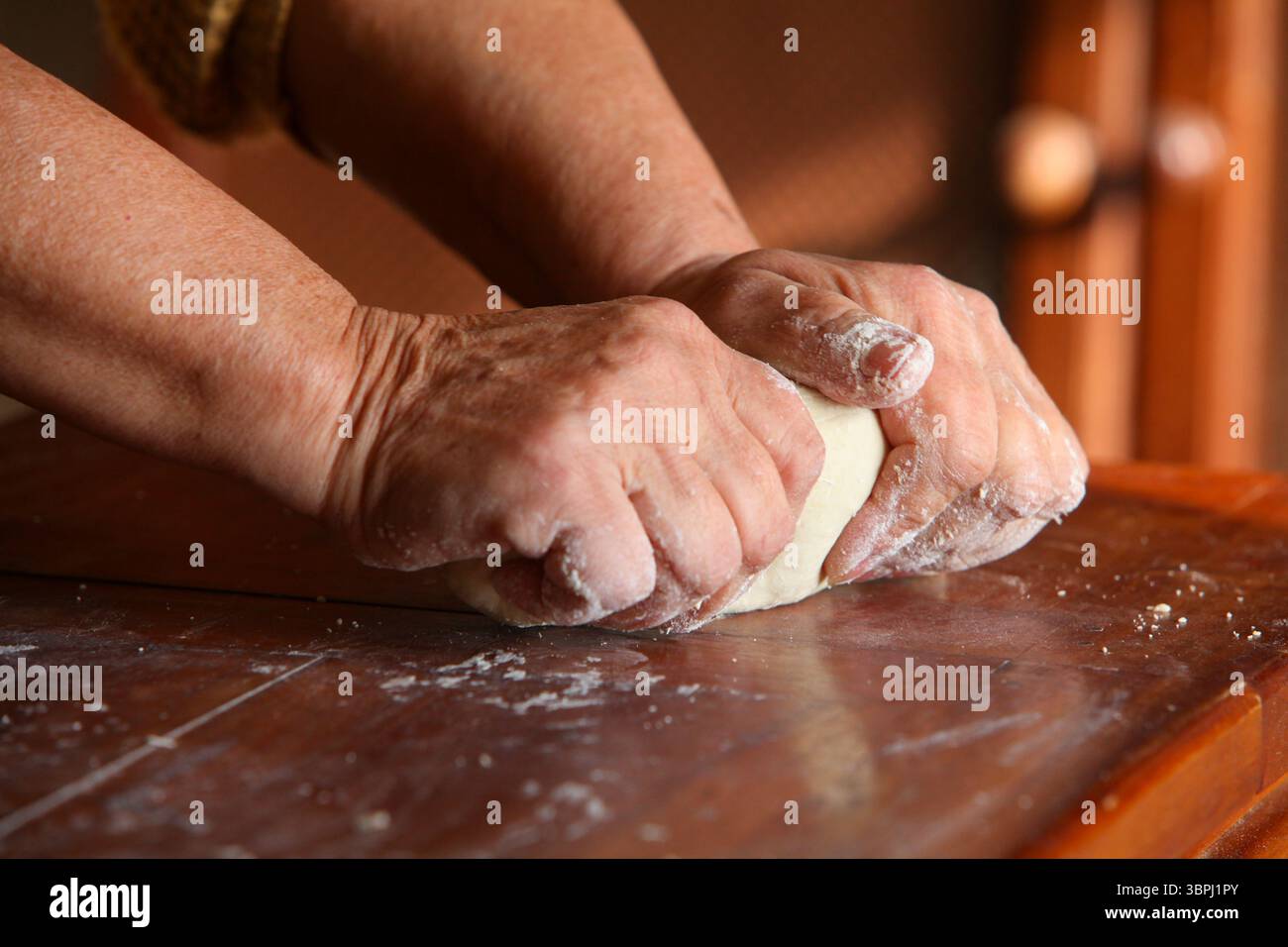 gros plan des mains d'une femme âgée, vêtue de façon désinvolte à la maison, faisant de la pâte à la main sur une table rustique en bois simple Banque D'Images