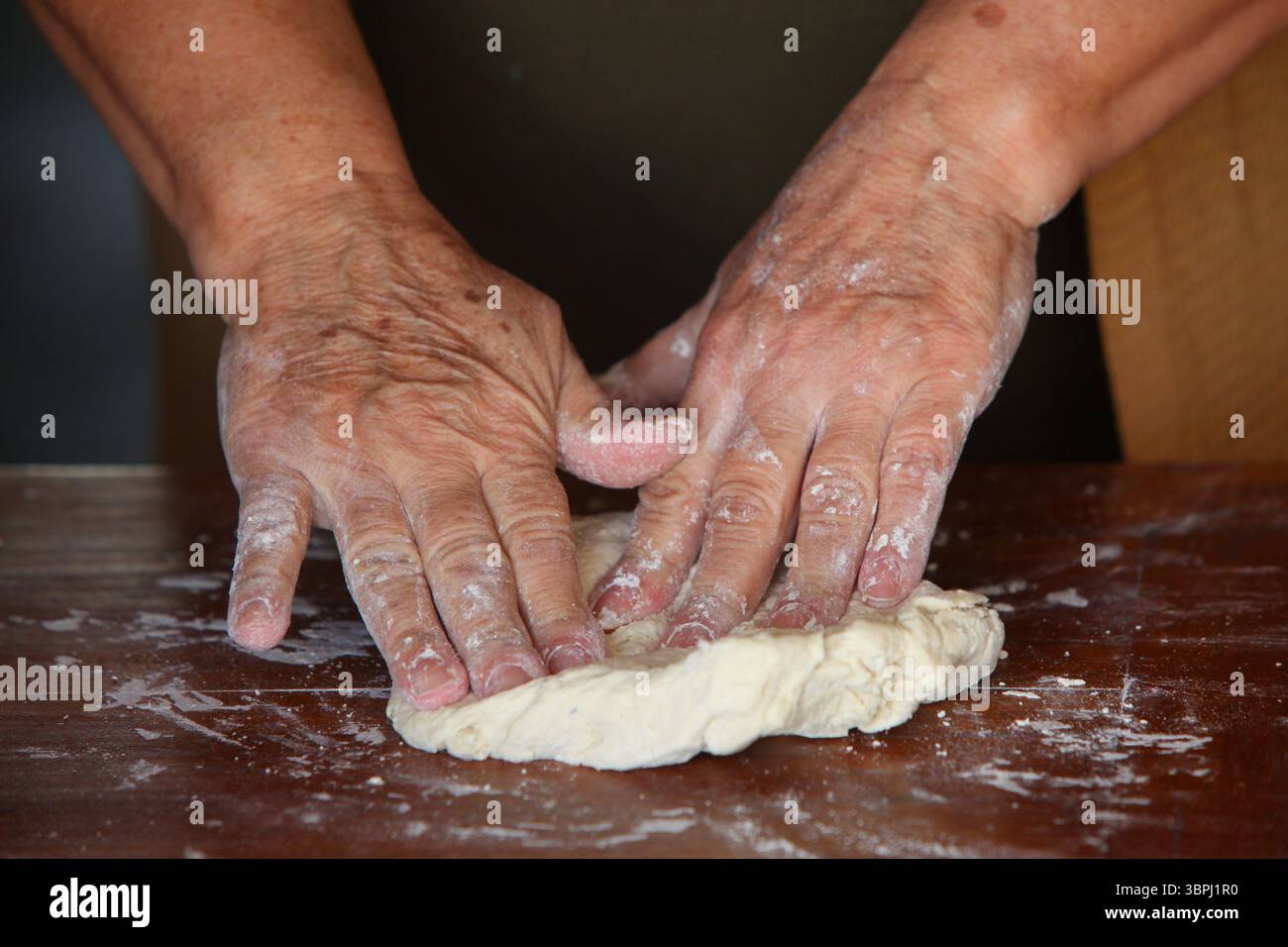 gros plan des mains d'une femme âgée, vêtue de façon désinvolte à la maison, faisant de la pâte à la main sur une table rustique en bois simple Banque D'Images