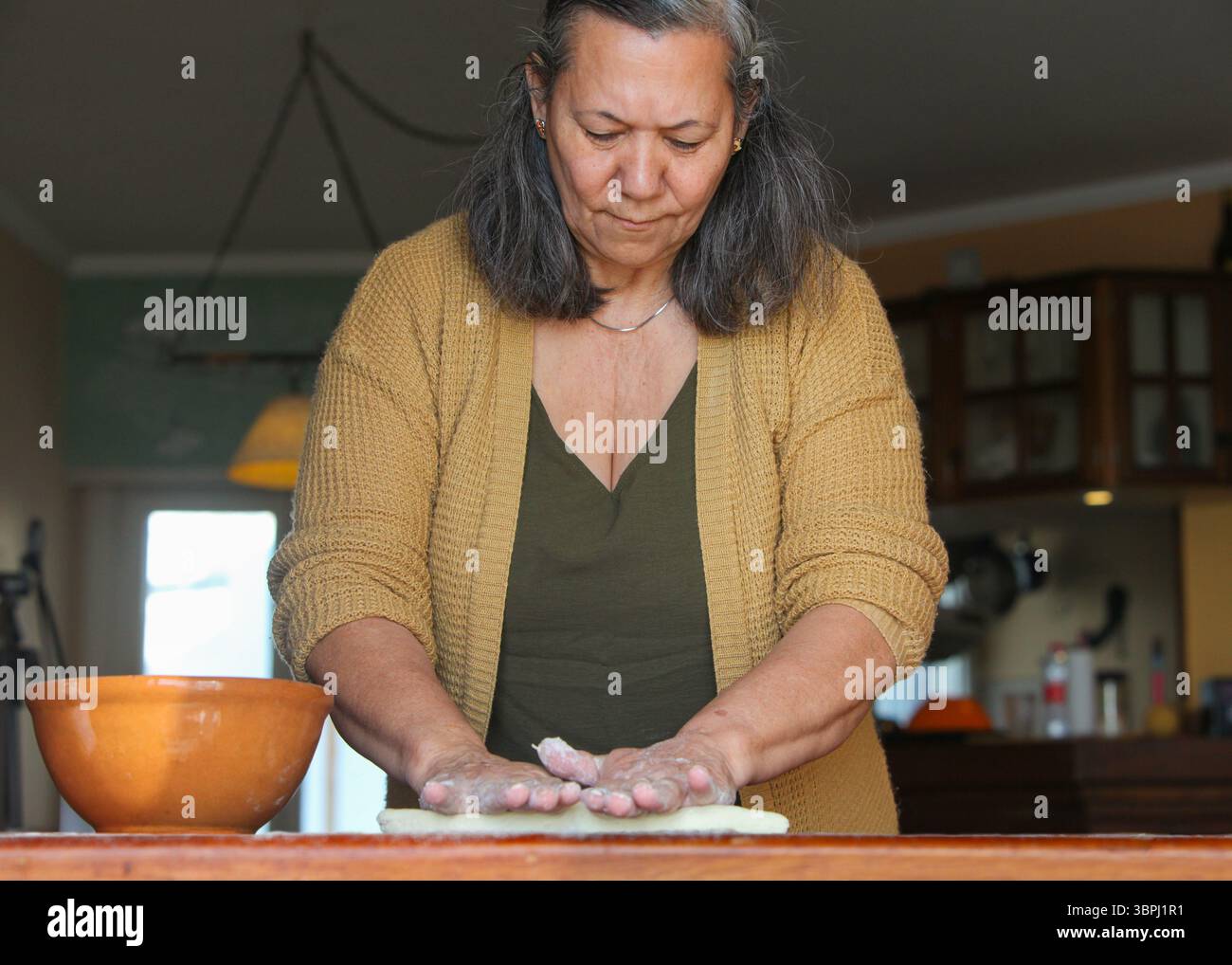 Mar del Plata. Buenos Aires.. Argentine. ..femme latina, dans ses 60 ans, habillée décontractée à la maison, faisant de la pâte à la main dans une cuisine simple. Banque D'Images