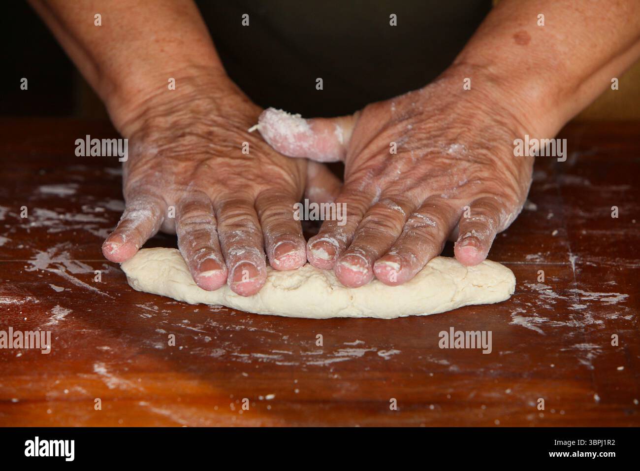 gros plan des mains d'une femme âgée, vêtue de façon désinvolte à la maison, faisant de la pâte à la main sur une table rustique en bois simple Banque D'Images