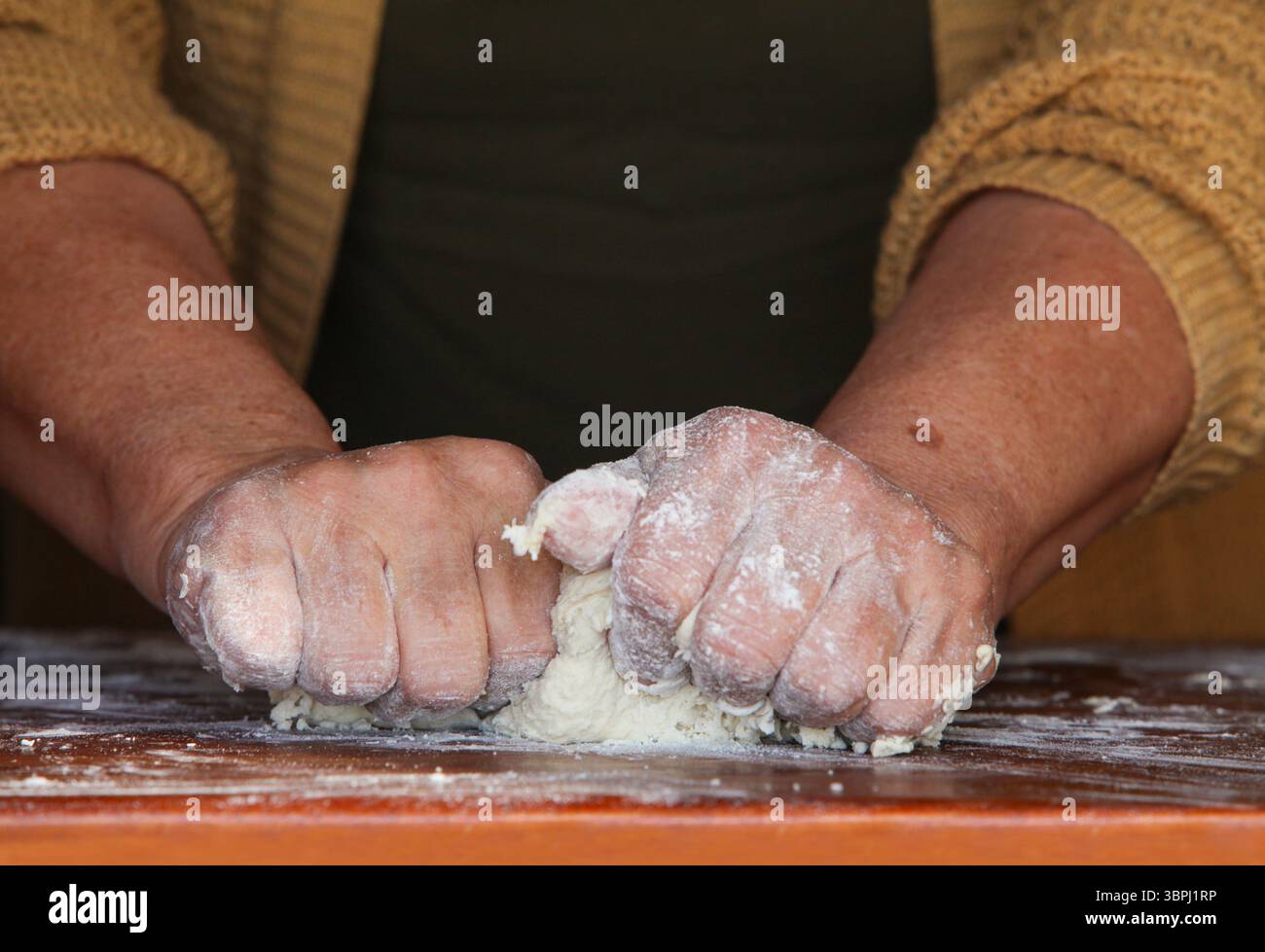 gros plan des mains d'une femme âgée, vêtue de façon désinvolte à la maison, faisant de la pâte à la main sur une table rustique en bois simple Banque D'Images