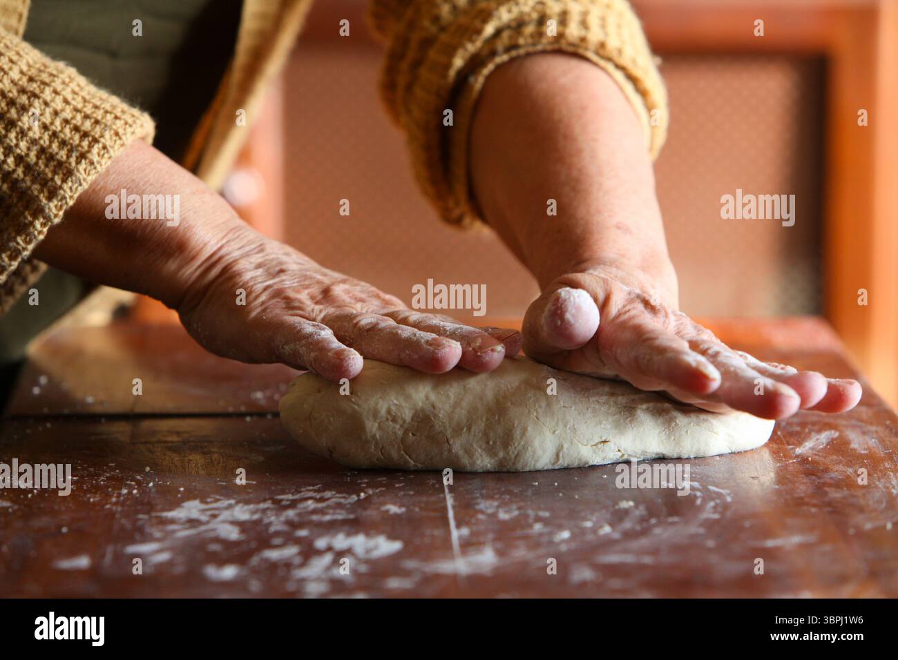 gros plan des mains d'une femme âgée, vêtue de façon désinvolte à la maison, faisant de la pâte à la main sur une table rustique en bois simple Banque D'Images