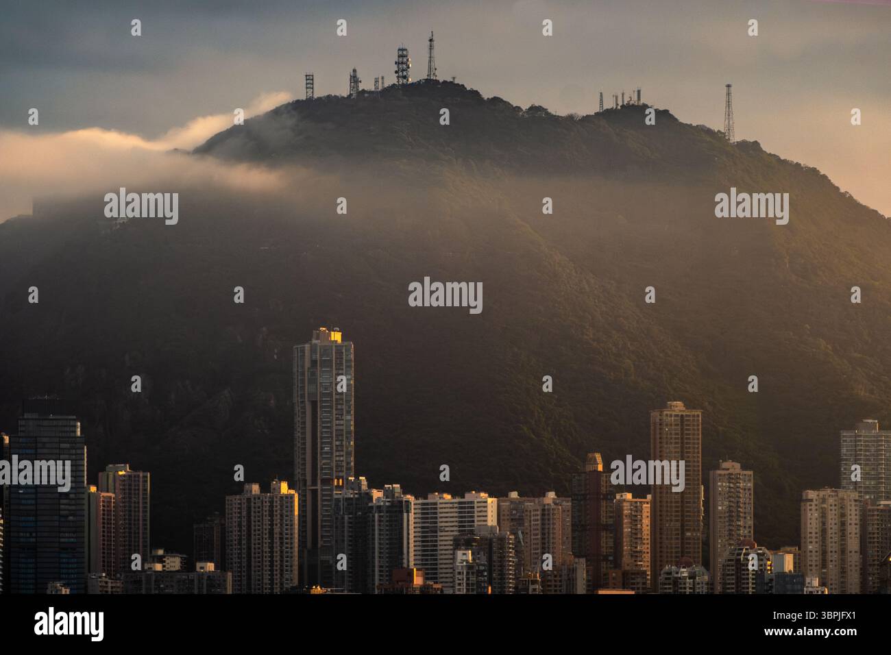 Bâtiments à Hong Kong avec une toile de fond de montagne pendant l'heure magique, éclairés par une lumière douce et chaude et partiellement enveloppés de brume. Banque D'Images