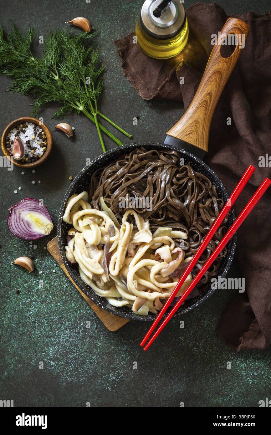 Nouilles épicées, cuisine traditionnelle coréenne. Nouilles de soba de sarrasin et calmars avec sauce à la crème aigre sur une table en pierre sombre. Vue de dessus de l'arrière-plan de la mise à plat Banque D'Images