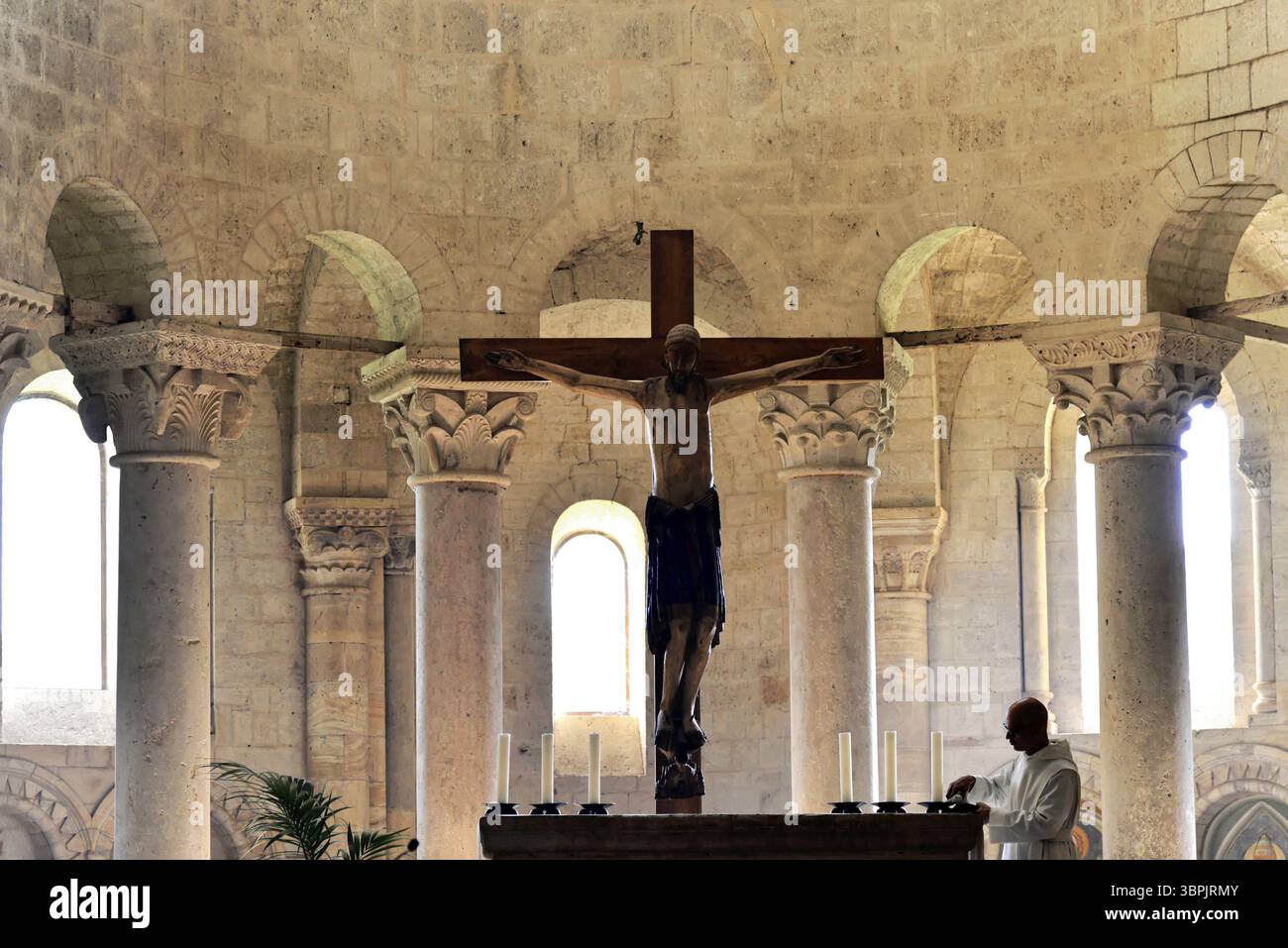 Un intérieur d'église avec une croix de Jésus, des bougies d'autel et un prêtre en arrière-plan, église abbatiale Abbazia di Sant'Antimo, près de Montalcino, province de Banque D'Images