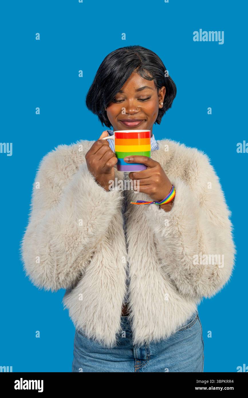 Portrait studio d'une jeune femme dégustant une boisson chaude d'une tasse arc-en-ciel, célébrant la fierté et la diversité Banque D'Images