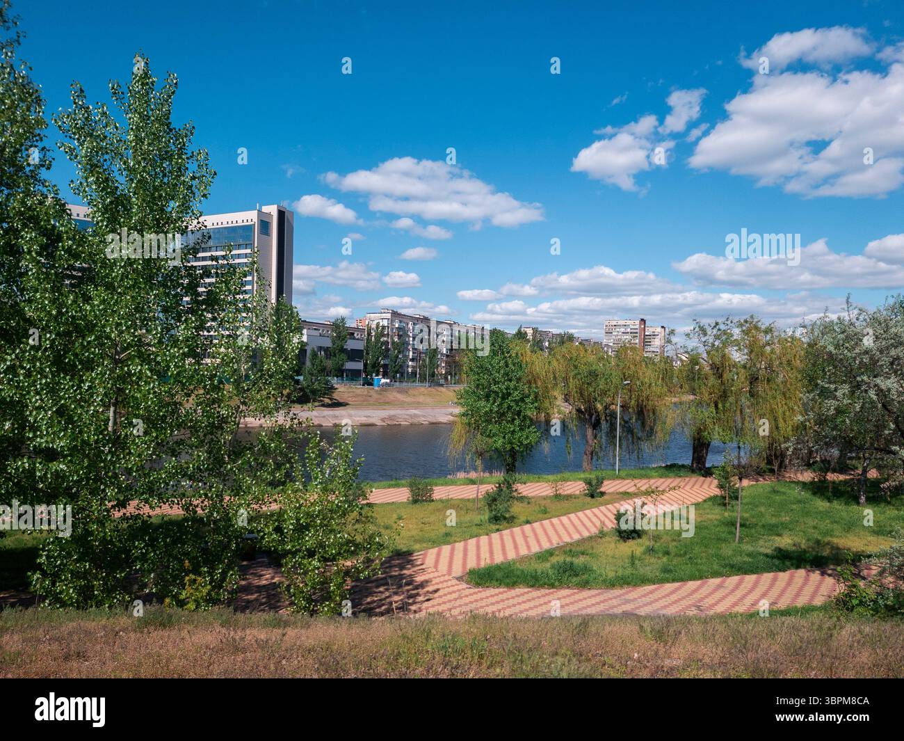 Le quartier résidentiel de Rusanivka présente un mélange d'espaces verts et de bâtiments modernes le long du canal de Dnipro sous un ciel bleu vif et des nuages dispersés Banque D'Images