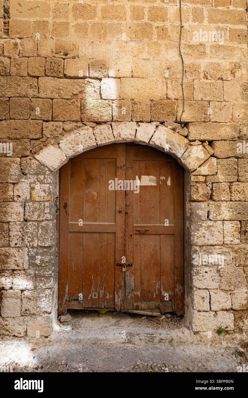 L'ancienne porte double en bois usée, située dans un mur de pierre rustique, affiche son charme historique et sa décadence architecturale. L'ancienne porte située à l'intérieur du h. Banque D'Images