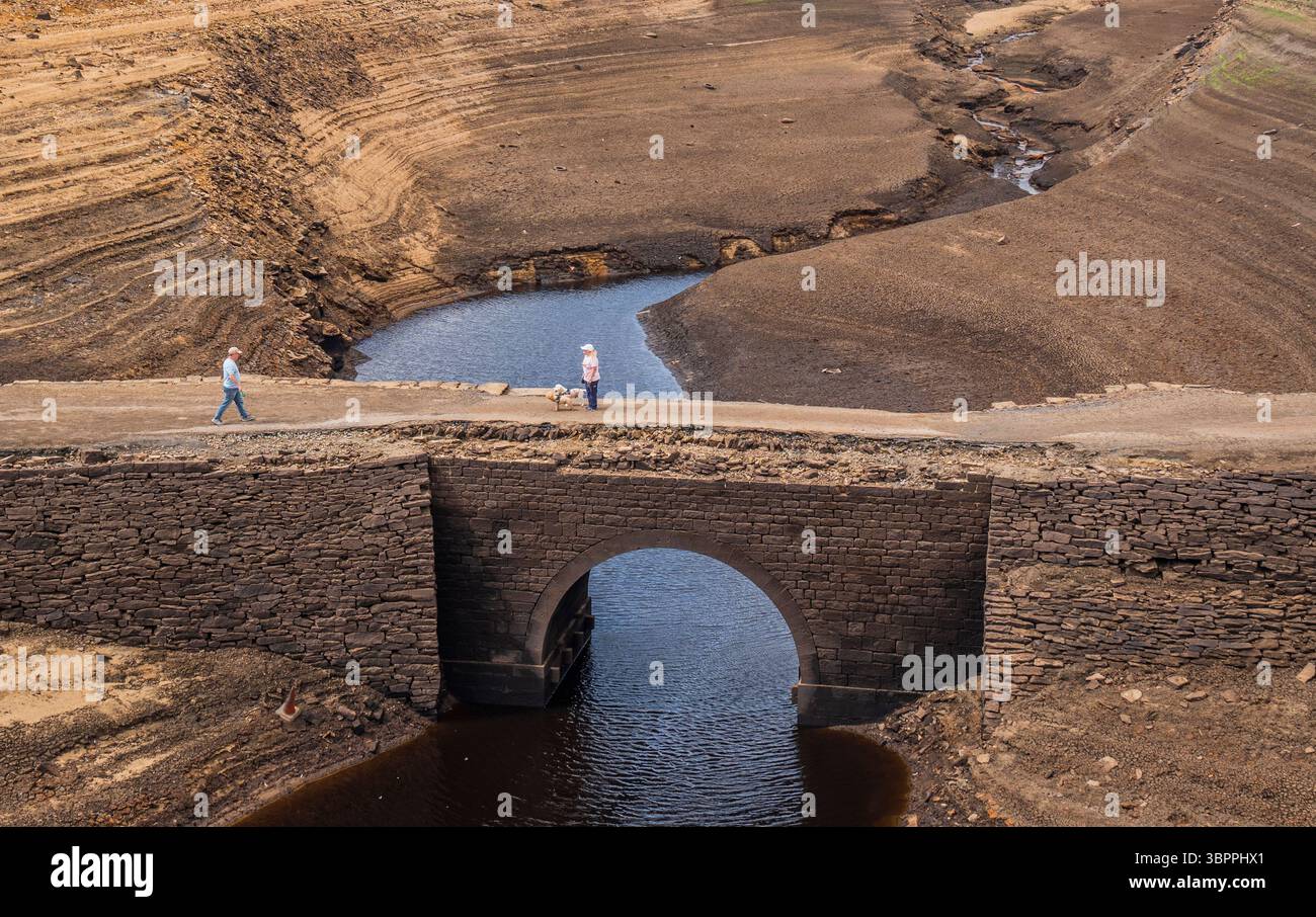 Les gens marchent sur un pont qui est normalement submergé par Baitings Reservoir à Ripponden, West Yorkshire. Les ménages du Yorkshire sont devenus les premiers à être frappés par une interdiction de canalisations par Yorkshire Water, après des mois de temps extrêmement chaud et sec à travers l'Angleterre. Date de la photo : mercredi 9 juillet 2025. Banque D'Images