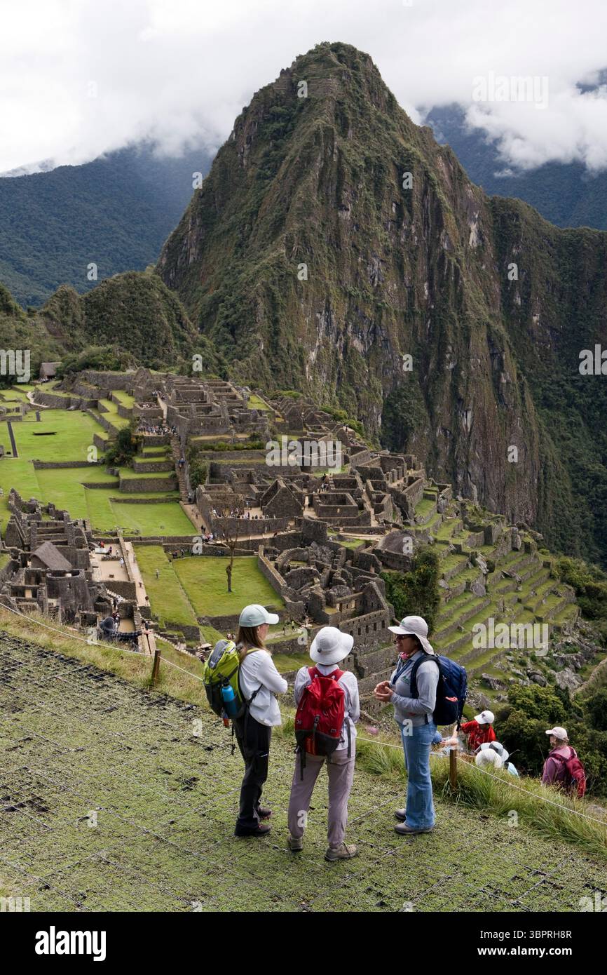Deux femmes touristes écoutent leur guide tout en surplombant Machu Picchu (avec la montagne Huayna Picchu derrière), Pérou. Banque D'Images