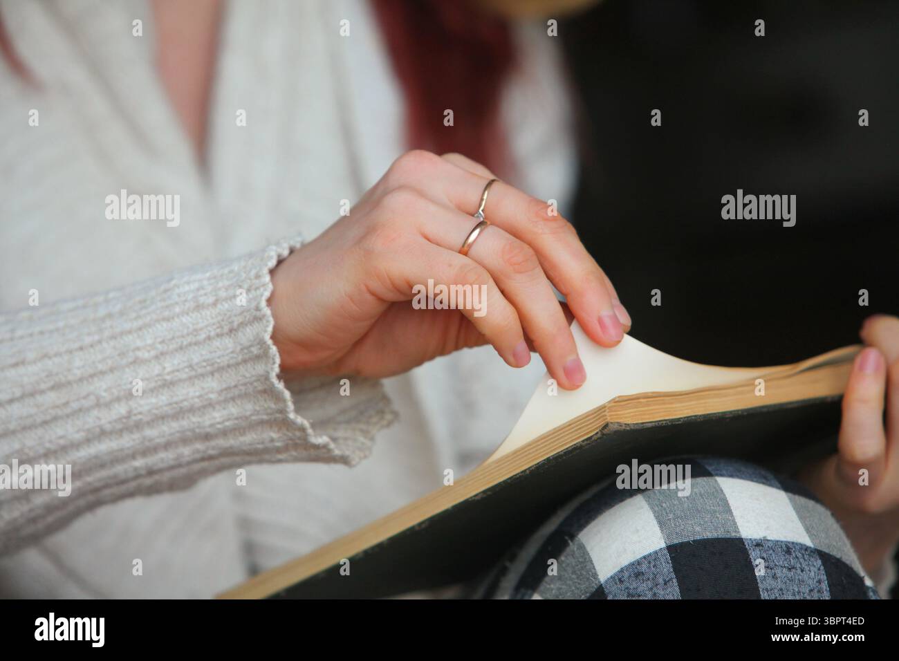 mains de femme, années 30, dans des vêtements de maison confortables, lisant un livre. Moment paisible et détendu à la lumière naturelle, ambiance printanière ou automnale. Banque D'Images
