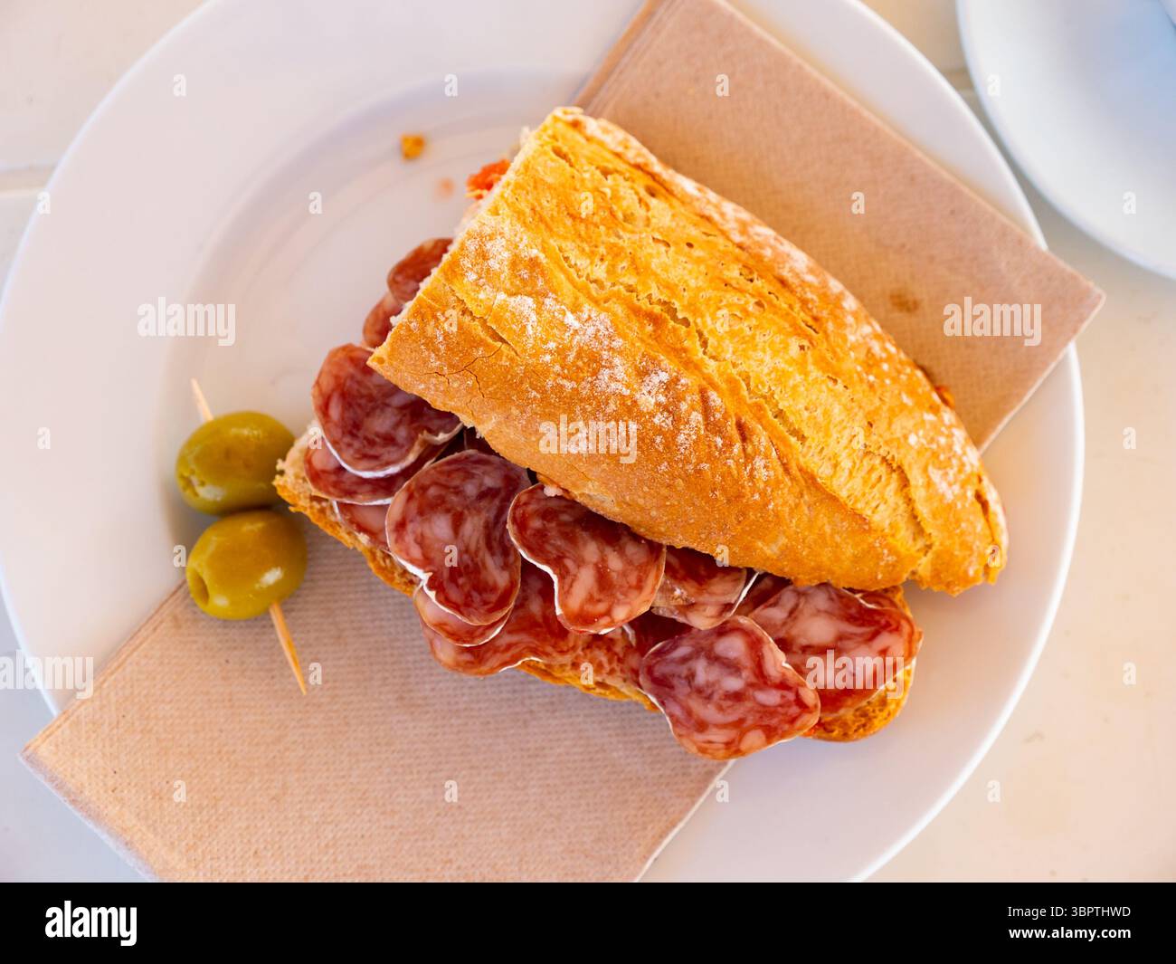 Petit-déjeuner espagnol - sandwich au fuet aux saucisses fumées et olives en gros plan Banque D'Images
