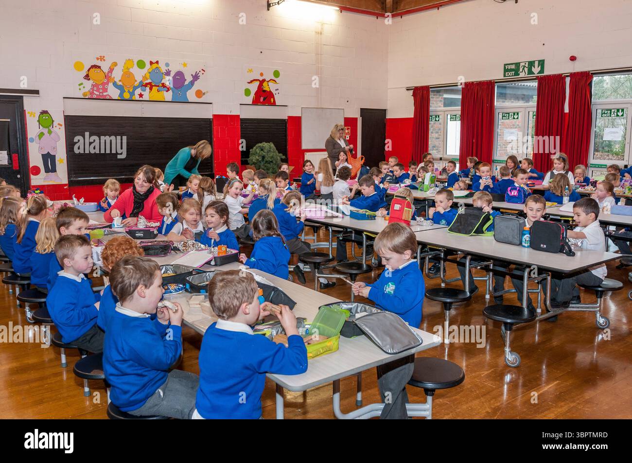 Les enfants de l'école primaire mangeant le déjeuner assis à des tables, Angleterre, Royaume-Uni Banque D'Images