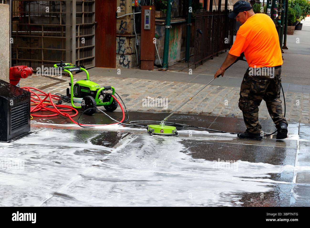 Un ouvrier lavant un trottoir de New York City avec un nettoyeur haute pression électrique Greenworks Pro 3000 psi Banque D'Images