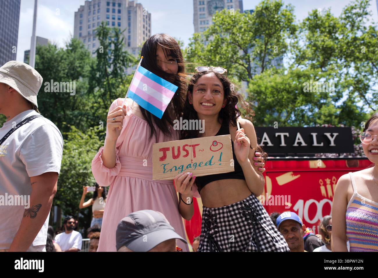 Deux femmes, l'une tenant un drapeau de fierté transgenre et l'autre tenant un "juste engagé !" signez, tenez-vous souriant ensemble à un événement en plein air. Ils sont su Banque D'Images