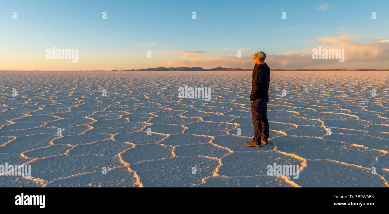 Coucher de soleil de désert plat de sel d'Uyuni avec des formations de sel hexagonales et un randonneur touriste masculin, Bolivie. Banque D'Images