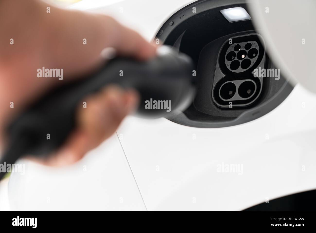 Vue rapprochée du port de charge et de la fiche du véhicule électrique sur le point d'être connectés à la main de l'utilisateur Banque D'Images