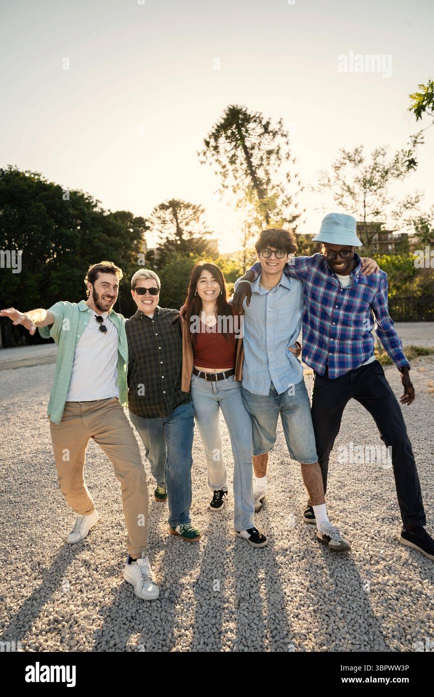 Un groupe multiethnique diversifié de jeunes amis avec leurs bras autour de l'autre, marchant ensemble sur un chemin au coucher du soleil. Repression verticale pleine longueur Banque D'Images