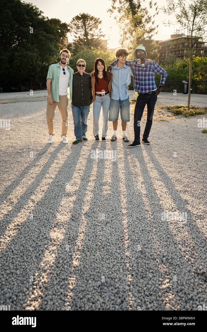 Un groupe multiethnique diversifié d'amis ou de collègues se tient ensemble, les bras autour l'un de l'autre, posant pour un portrait d'équipe à l'extérieur au coucher du soleil Banque D'Images