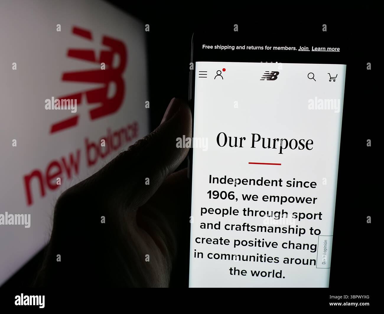 Stuttgart, Allemagne - 05-07-2025 : personne tenant un téléphone portable avec la page web de la société américaine New Balance Athletics Inc (NB) sur l'écran devant le logo. Banque D'Images
