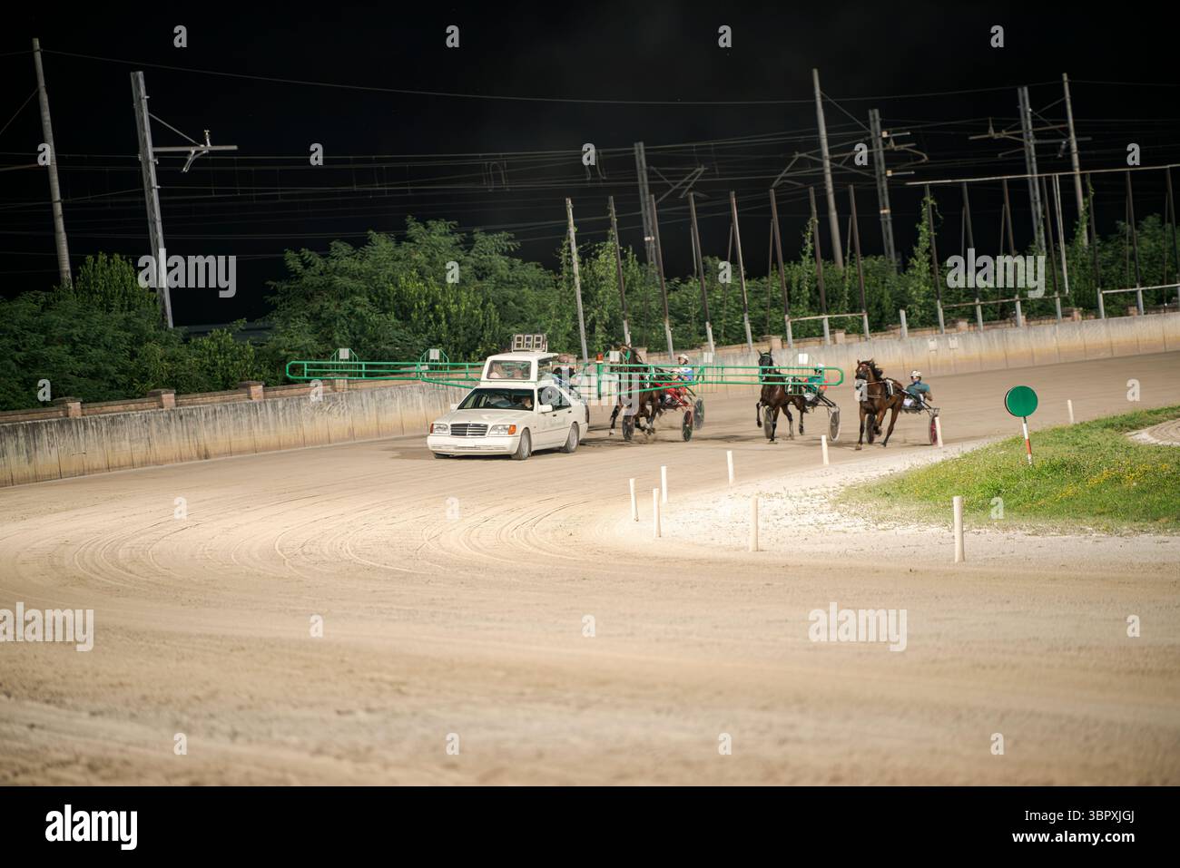 Padoue, italie 8 juillet 2025, événement passionnant de course harnais la nuit avec des chevaux et des pilotes suivant une voiture pilote sur une piste de terre sous des lumières vives et Banque D'Images