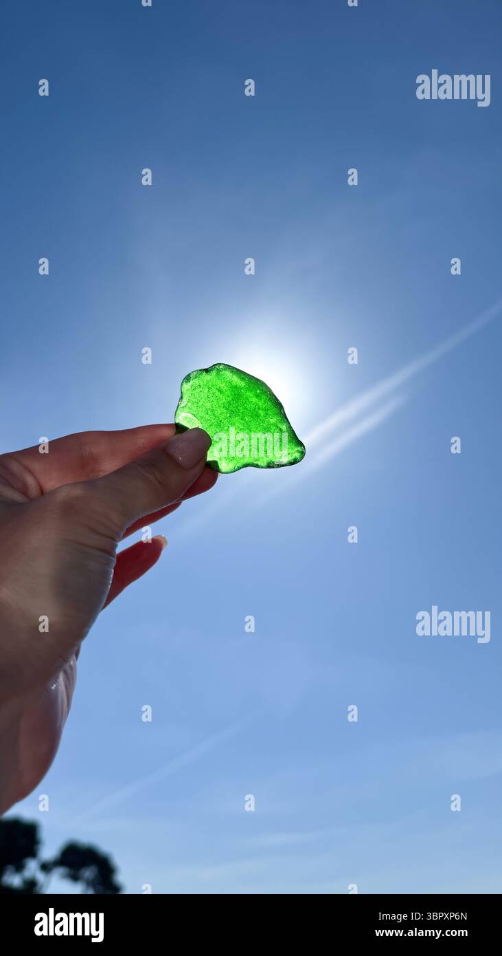 Un morceau de verre de mer vert tenu dans une main, illuminé par la lumière du soleil avec l'océan en arrière-plan. Un symbole de nature, de simplicité et d'été Banque D'Images