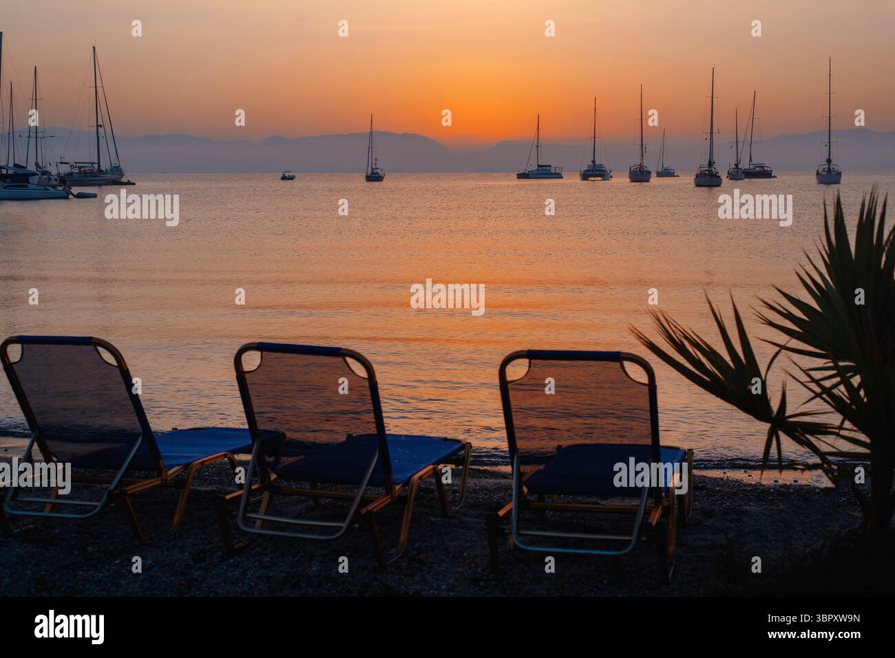 Deux transats debout sur la plage tropicale au coucher du soleil. Silhouette de bateaux sur la mer pendant le coucher du soleil. Photo de stock Banque D'Images