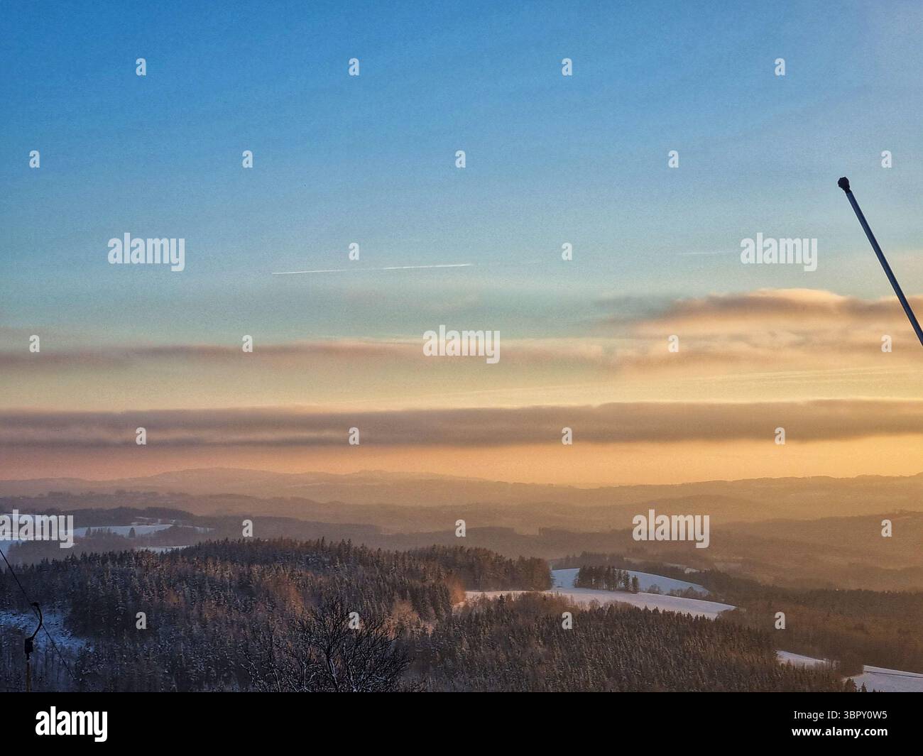 Le coucher de soleil hivernal vibrant peint le ciel nuageux orange et rose sur un paysage de montagne enneigé avec un pylône de remontée mécanique isolé dans une station de ski tchèque tranquille. - Image de stock capturée avec un smartphone