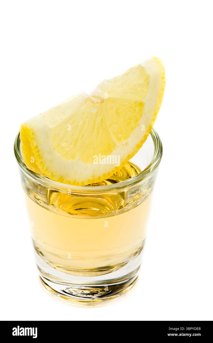 tequila tourné dans un petit verre avec une tranche de citron sur le dessus sur fond blanc Banque D'Images