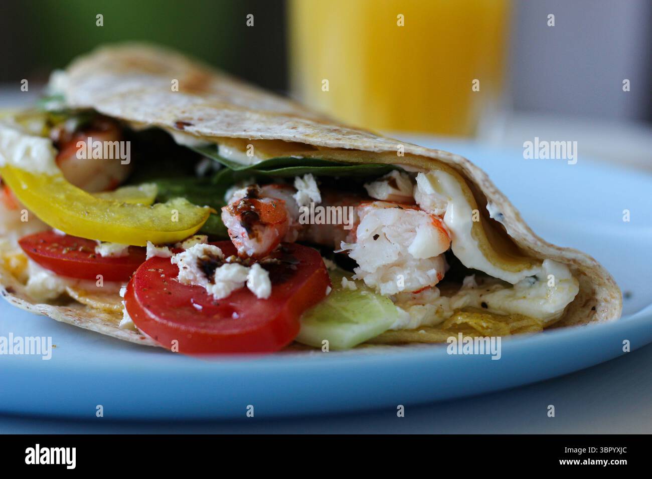Gros plan d'une tortilla pliée à base d'oeuf, montrant du fromage crémeux, des crevettes, de l'avocat et des épinards frais. Textures riches d'un petit déjeuner sain Banque D'Images