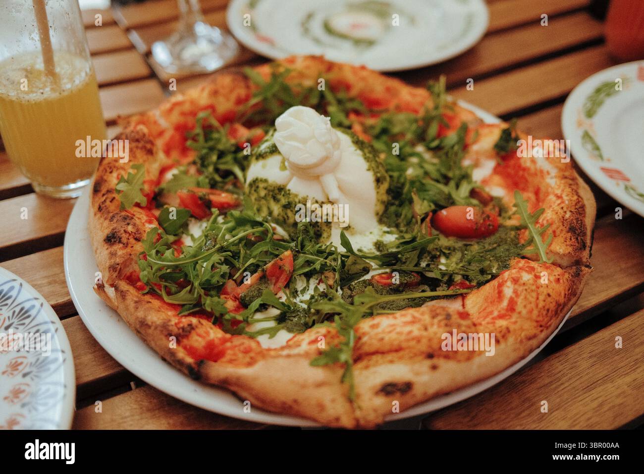 Pizza fraîchement cuite garnie de burrata crémeuse, de tomates et de feuilles de rucola fraîches Banque D'Images Pizza fraîchement cuite garnie de burrata crémeuse, de tomates et de feuilles de rucola fraîches Banque D'Images