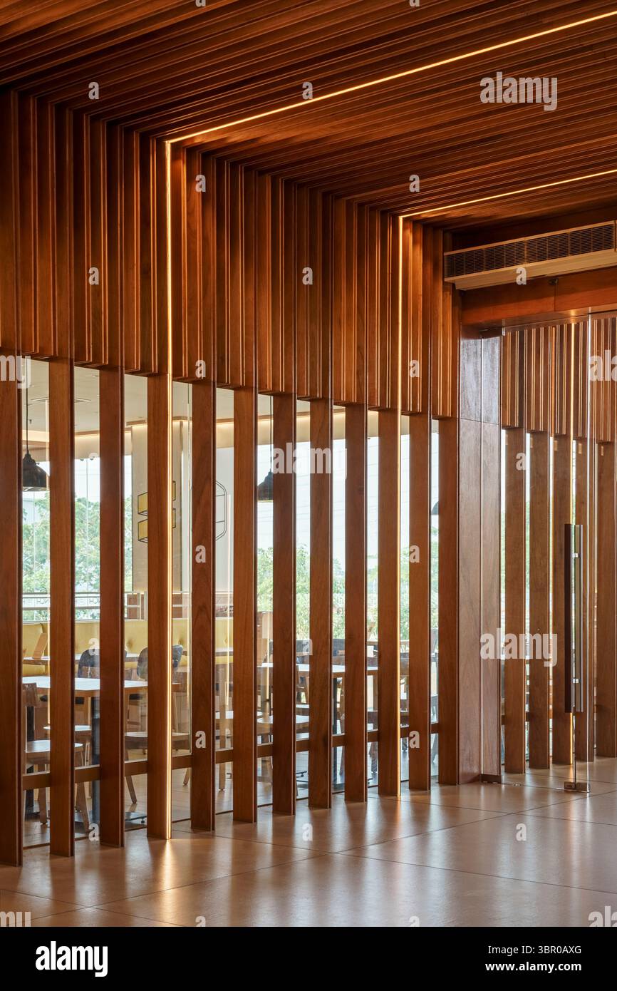 L'intérieur moderne du restaurant comprend un mur de séparation à lamelles en bois avec miroir intégré et un éclairage LED chaud. Banque D'Images