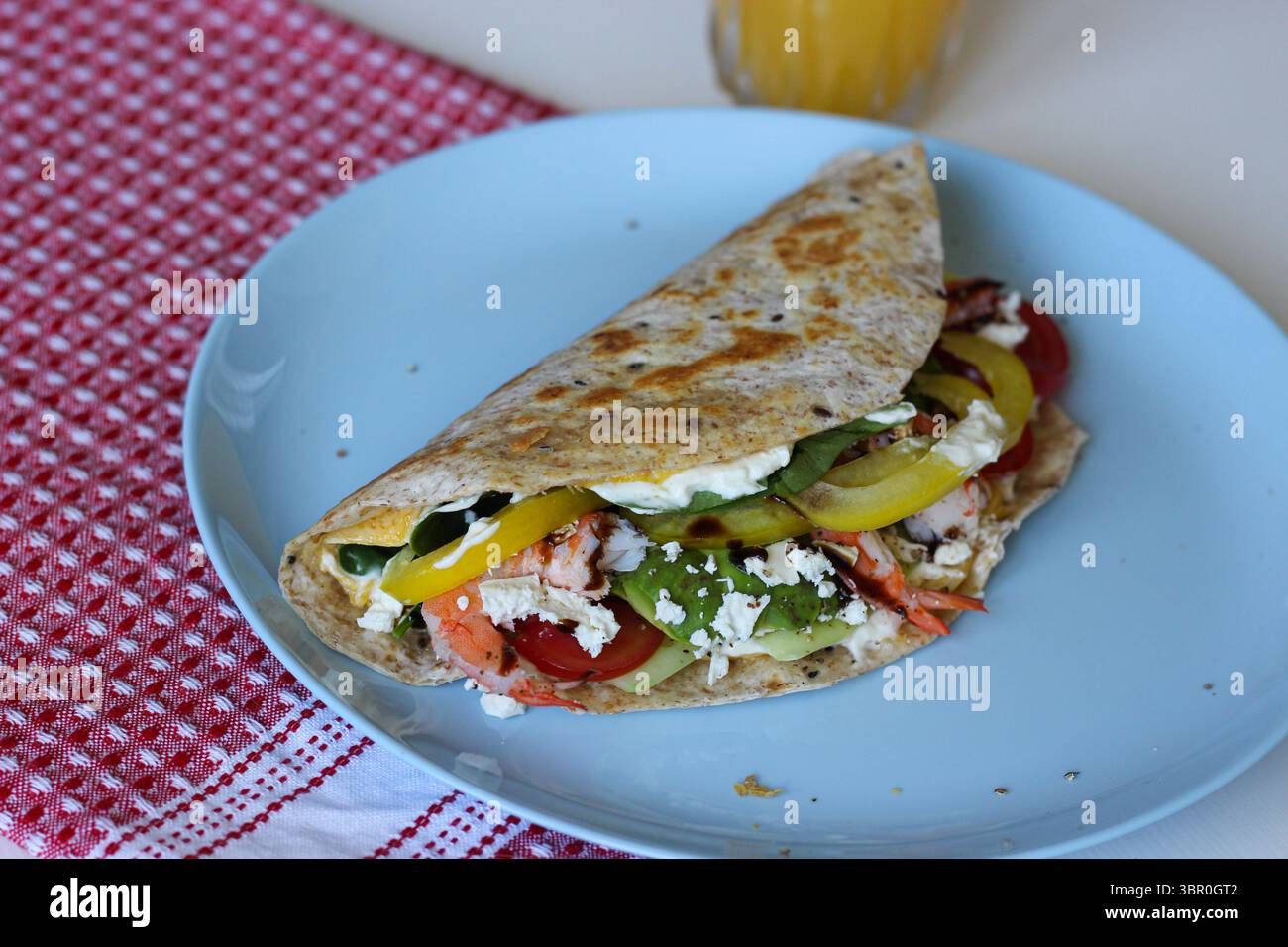 Vue de côté de l'enveloppe tortilla aux œufs pliés remplie de crevettes, d'avocat, d'épinards, de feta et de légumes. Petit déjeuner maison nutritif sur une assiette bleue Banque D'Images