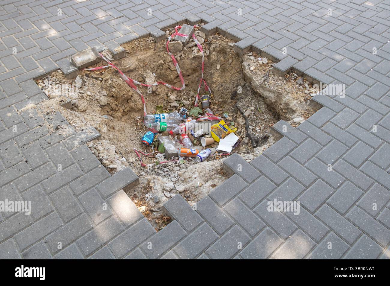Chisinau, Moldavie - 01 juin 2025 - tas de déchets jetés dans un trou de trottoir ouvert pendant des travaux de construction dans la rue publique. Banque D'Images
