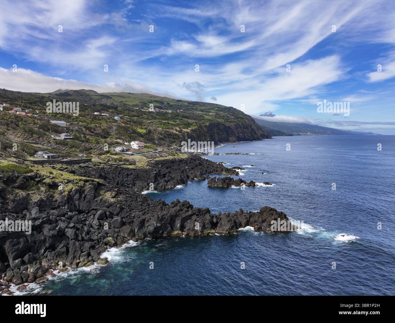 Vue aérienne des formations rocheuses de lave noires dures rencontrent la mer bleue profonde sous un ciel strié de nuages sinueux, cratère volcanique Pico, Açores, Portugal. Banque D'Images