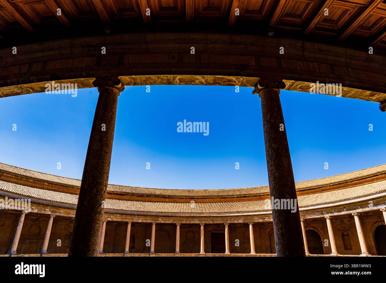 Colonnade en pierre Renaissance du Palais Charles V dans l'Alhambra, encadrée sous le portique à caissons et contre un ciel andalou vif Banque D'Images