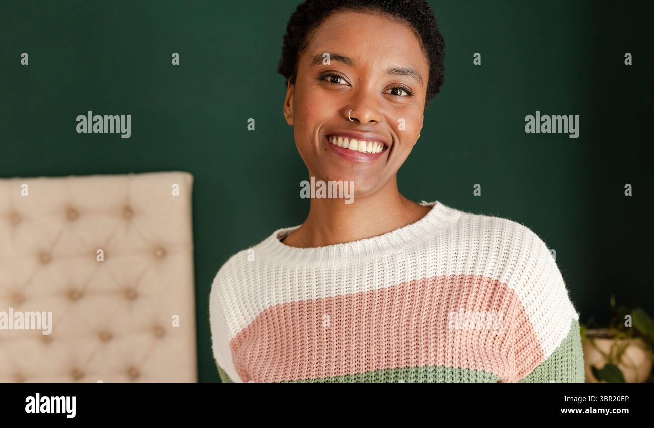 Femme afro-américaine souriant à la caméra dans la chambre près de la tête de lit avec plante en pot, espace de copie. Portrait, bien-être, confortable, décoration intérieure, lighti naturel Banque D'Images