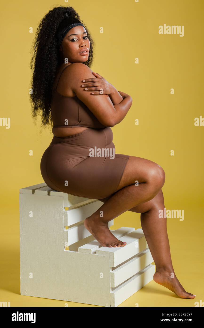 Femme afro-américaine posant en tenue marron sur la plate-forme en studio avec bandeau noir. Mode, fitness, vêtements d'activité, minimaliste, bien-être, empowerme Banque D'Images