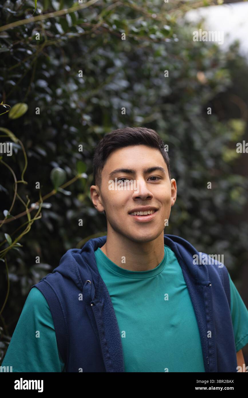 Homme hispanique debout sur le chemin du jardin souriant à la caméra portant un t-shirt sarcelle et un sweat à capuche bleu marine. Portrait, nature, extérieur, décontracté, verdure, bien-être, lif Banque D'Images