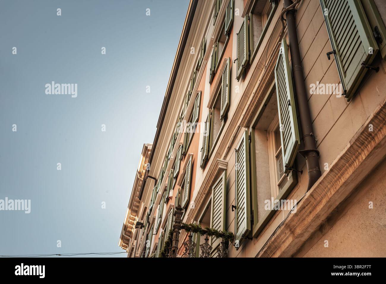 Vue vers le haut de la façade pastel dans la vieille ville de Trieste, en Italie, avec des rangées étagées de volets ouverts en bois vert, balcon orné de ferronnerie décorée de g. Banque D'Images