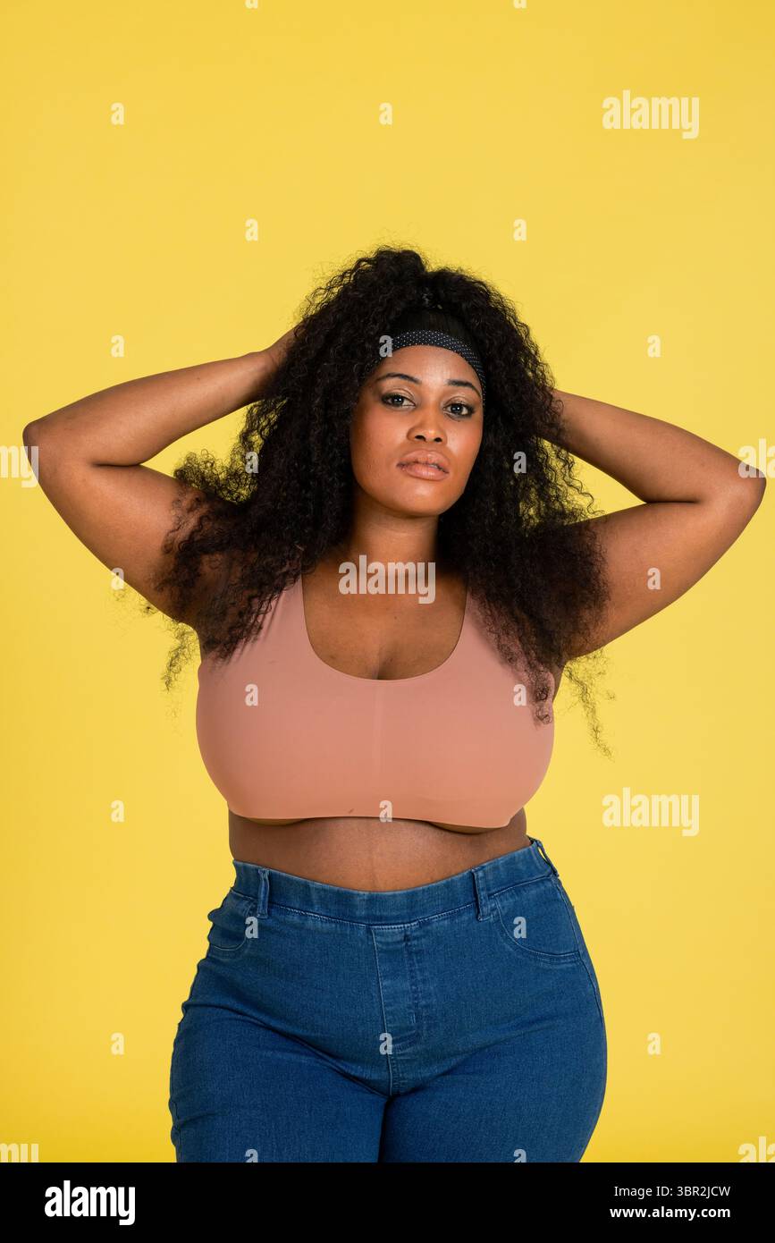 Femme afro-américaine posant sur fond de studio jaune portant bandeau noir, soutien-gorge et jeans Banque D'Images