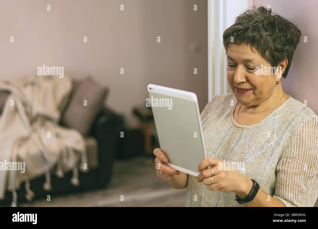 Belle femme sénior élégante restant près du mur et utilisant une tablette à la maison Banque D'Images
