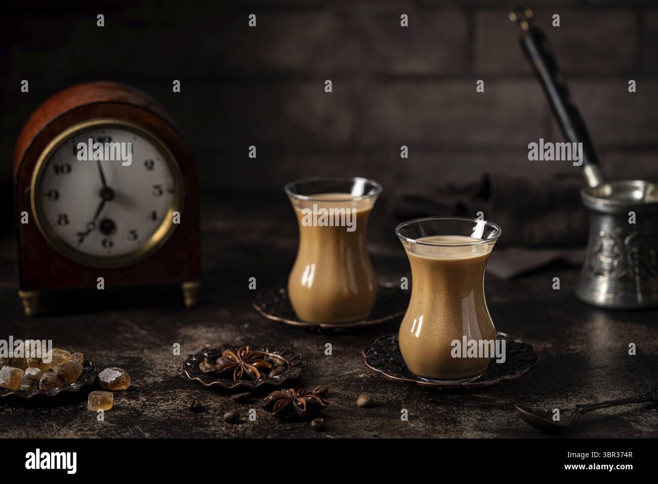 Thé ou café avec du lait et des épices en verre Armudu avec des grains de café et du sucre sur fond sombre Banque D'Images