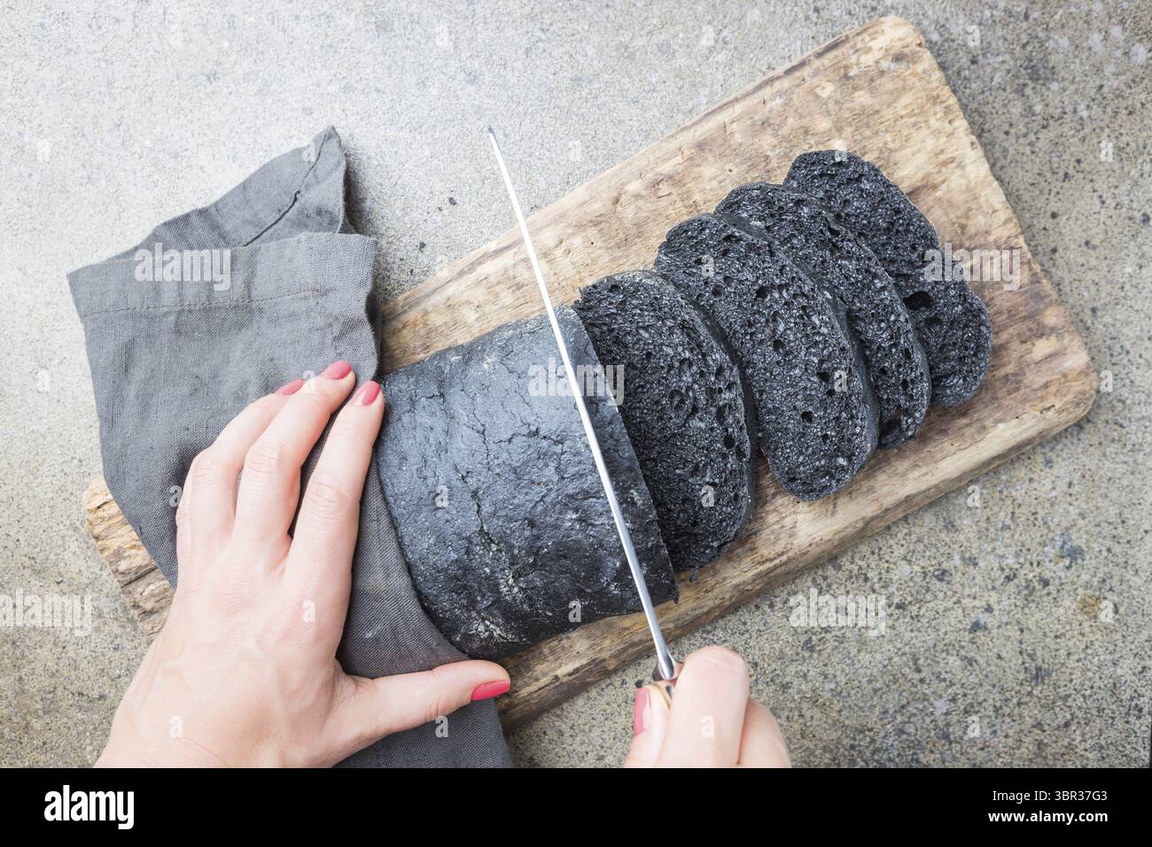 Tranches de pain noir coloré avec l'encre de seiche sur fond gris avec femme mains, vue d'en haut Banque D'Images