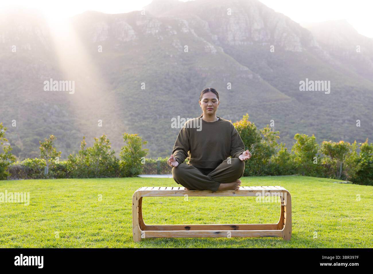 Femme asiatique assise aux jambes croisées méditant sur un banc en bois dans le jardin surplombant la crête de la montagne Banque D'Images